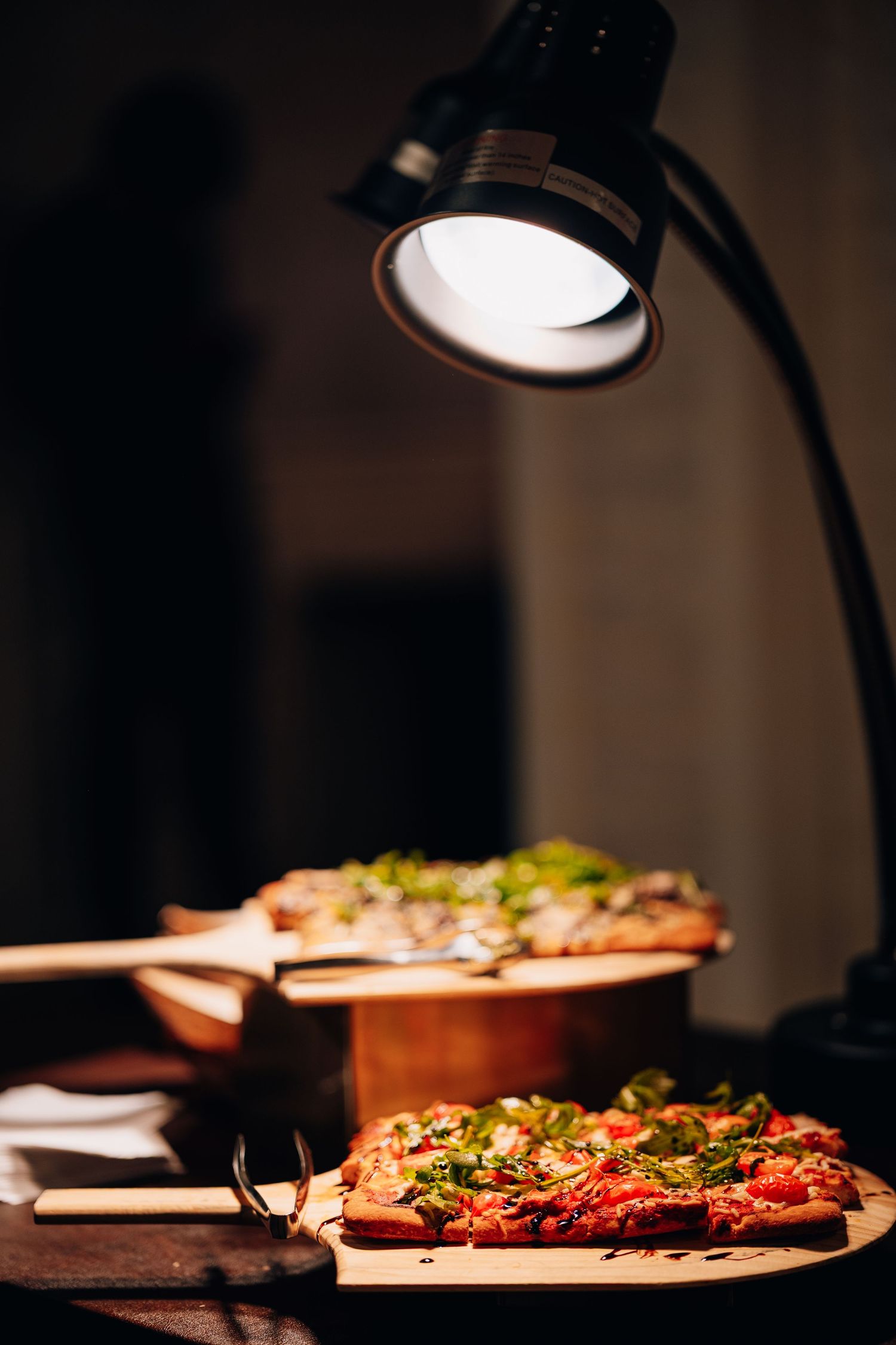 Sliced pizza topped with fresh arugula displayed under warm lamp at catering station.