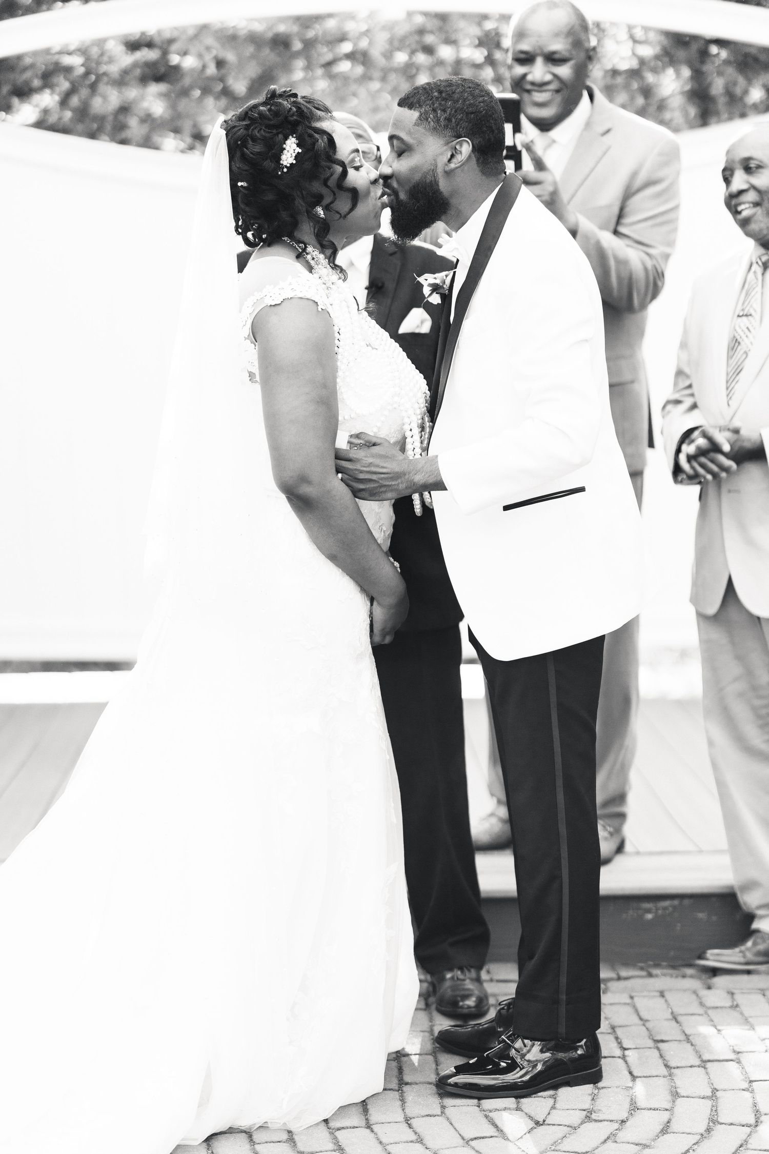 Black and white photo of bride and groom sharing first kiss at wedding ceremony.