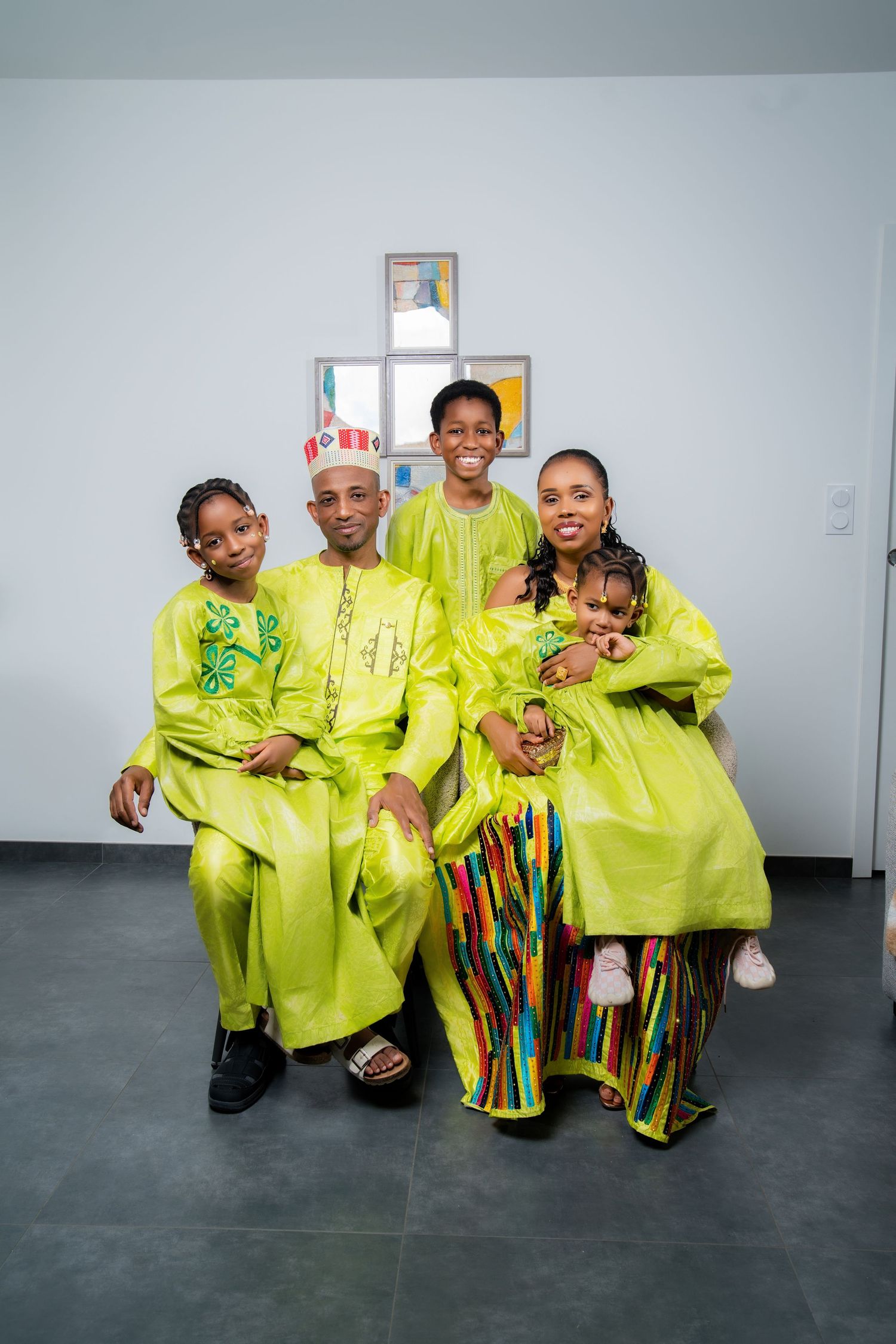 A joyful African family of five wearing matching bright green traditional attire poses together indoors.