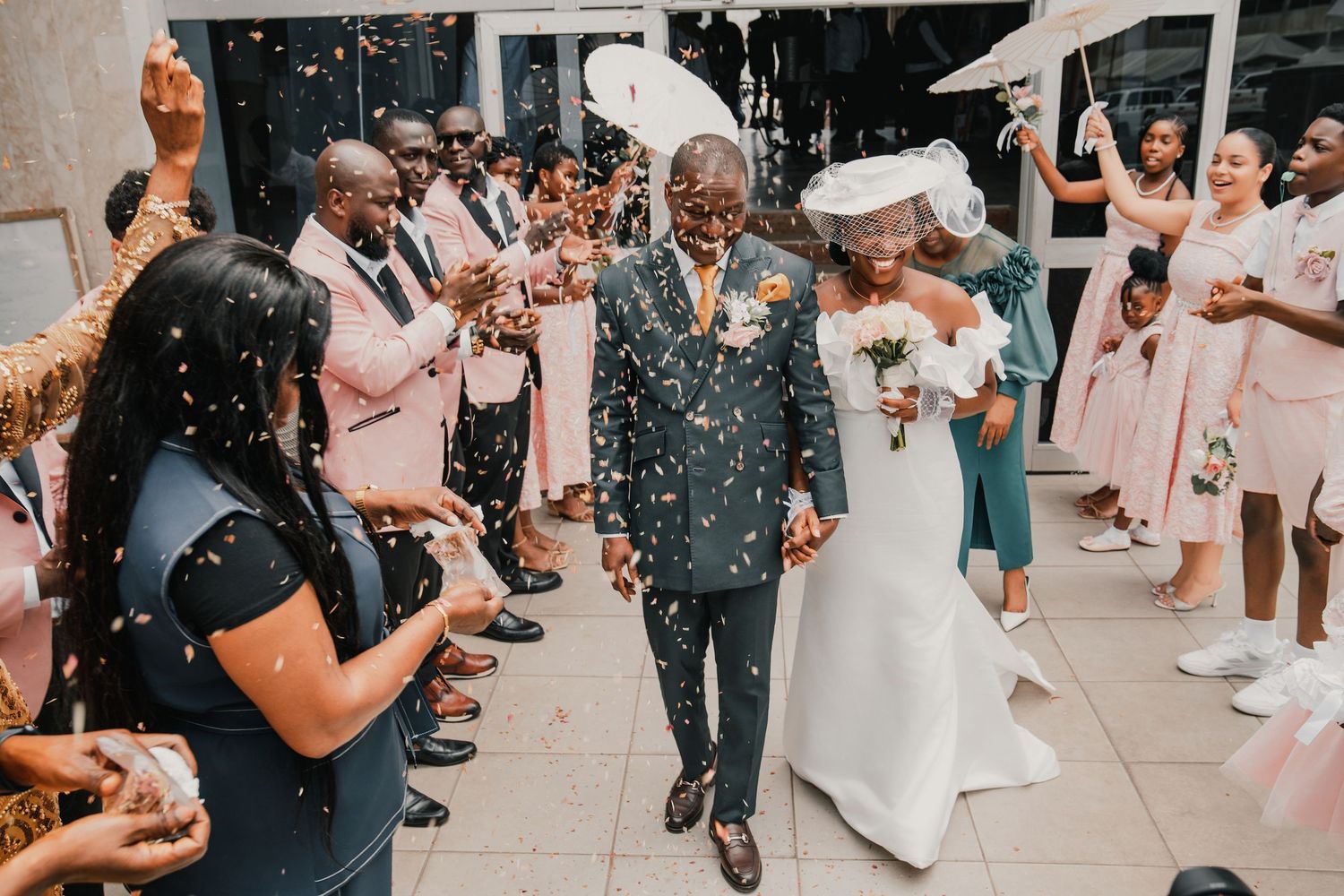 Joyful newlyweds walk through confetti shower surrounded by celebrating guests at elegant wedding reception.