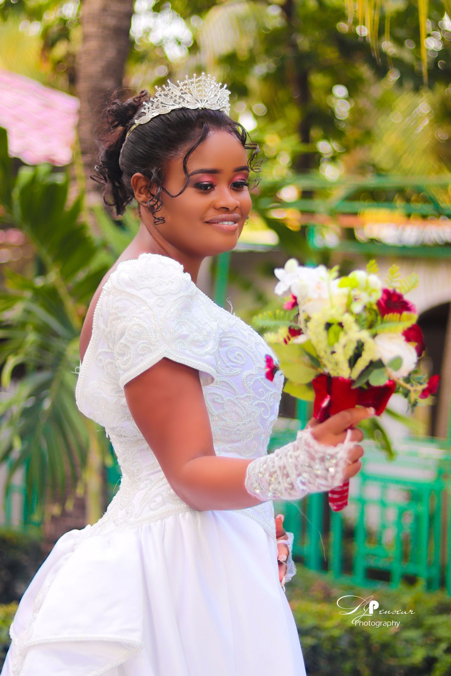 Bridal portrait in white dress with tiara holding bouquet in tropical garden setting.