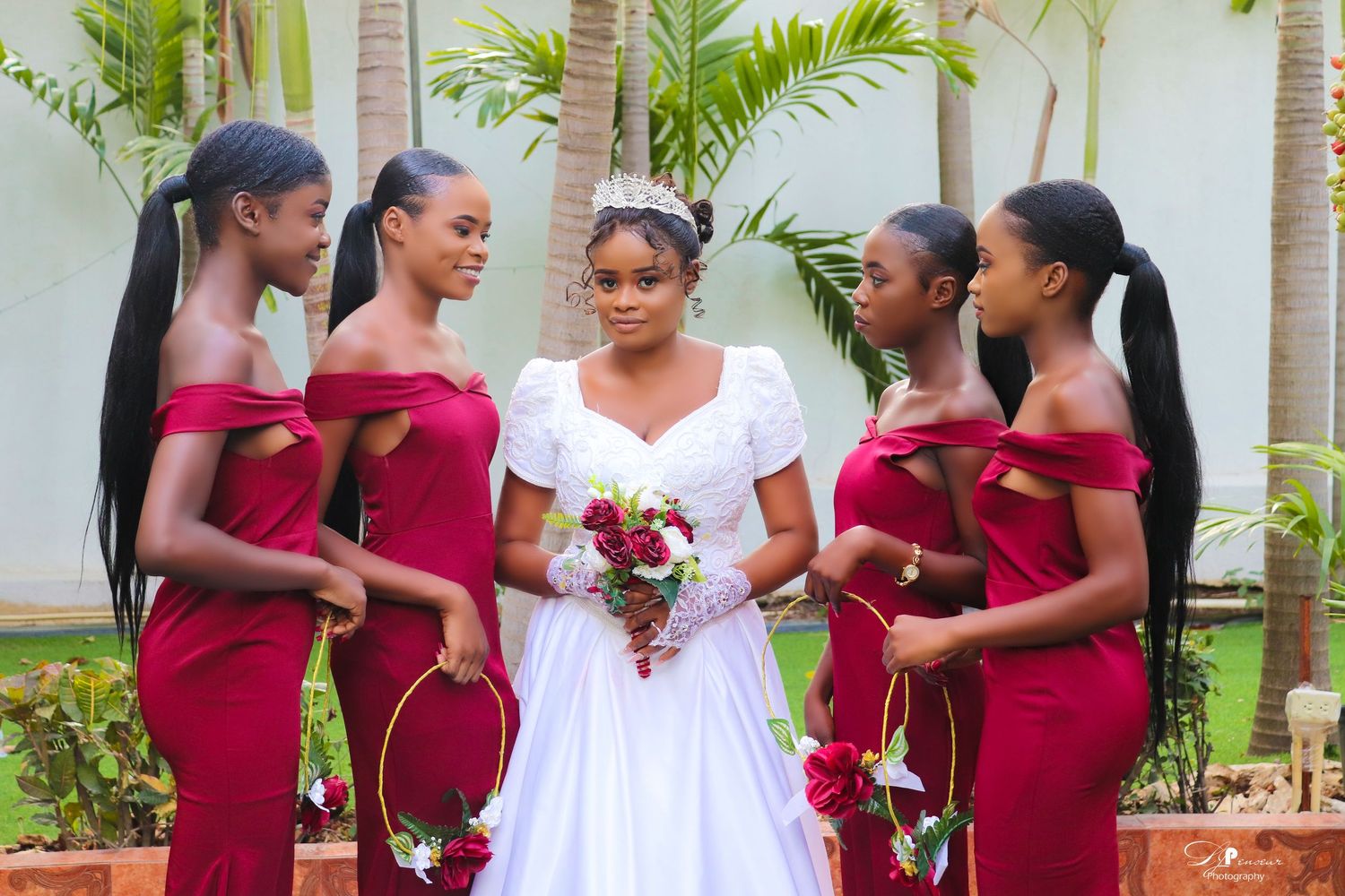 Wedding party in white and burgundy dresses posing together in tropical garden setting.