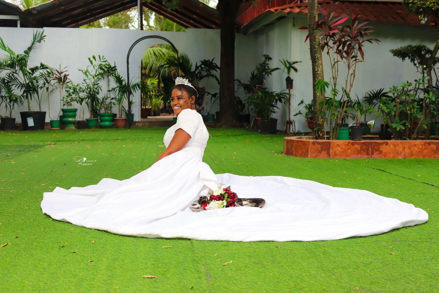Wedding photo of person in flowing white dress posed on green lawn with tropical plants.