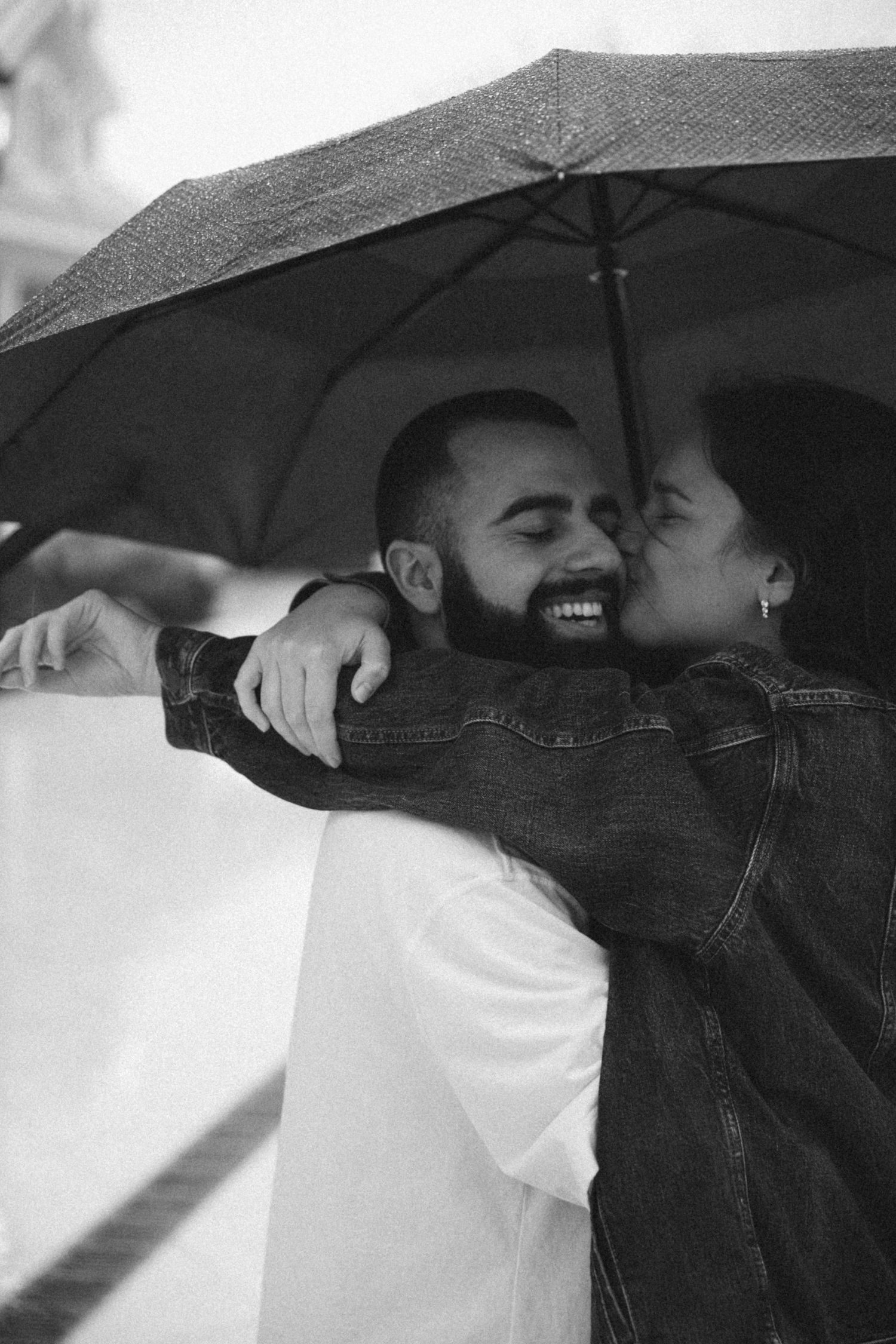 A romantic black and white moment captured under an umbrella on a rainy day.