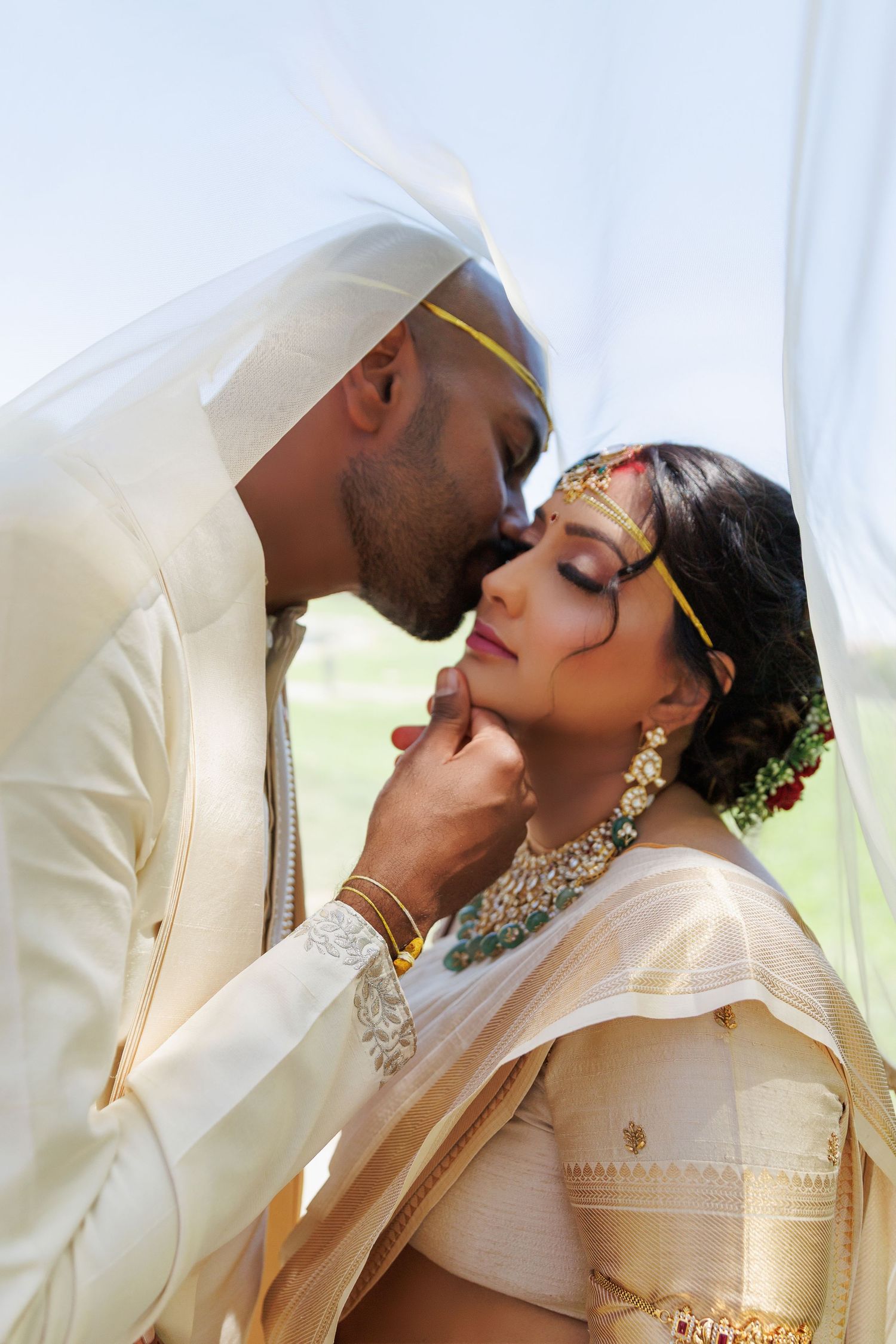 Indian bride and groom in traditional wedding attire share a romantic moment, groom kissing bride on forehead.