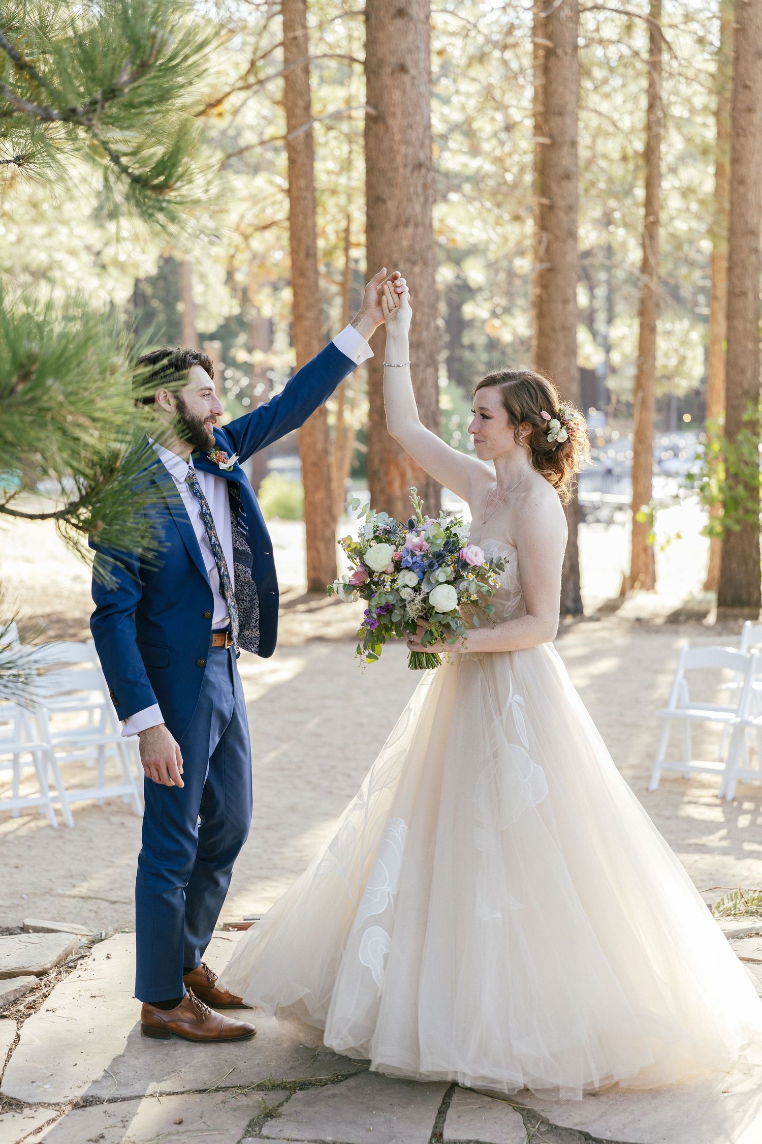 Wedding couple celebrates with joyful poses and gestures in a pine forest setting.