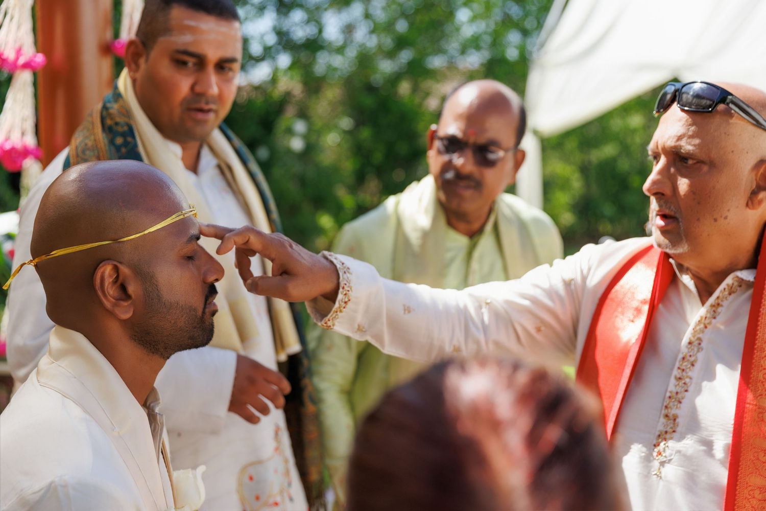 Traditional Indian wedding ceremony with groom receiving tilak blessing from elder outdoors.