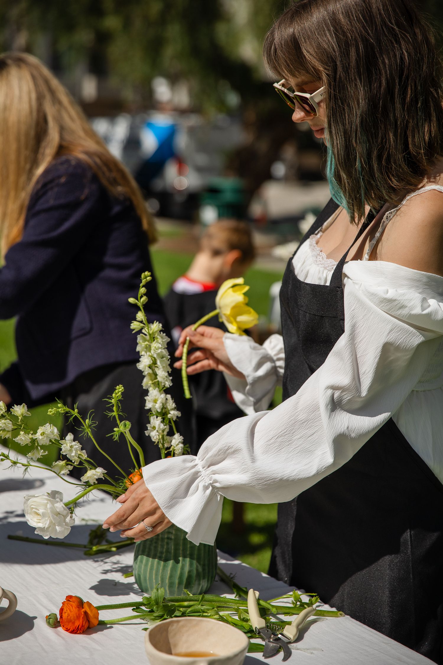 People in black and white attire arrange flowers at an outdoor workshop table.