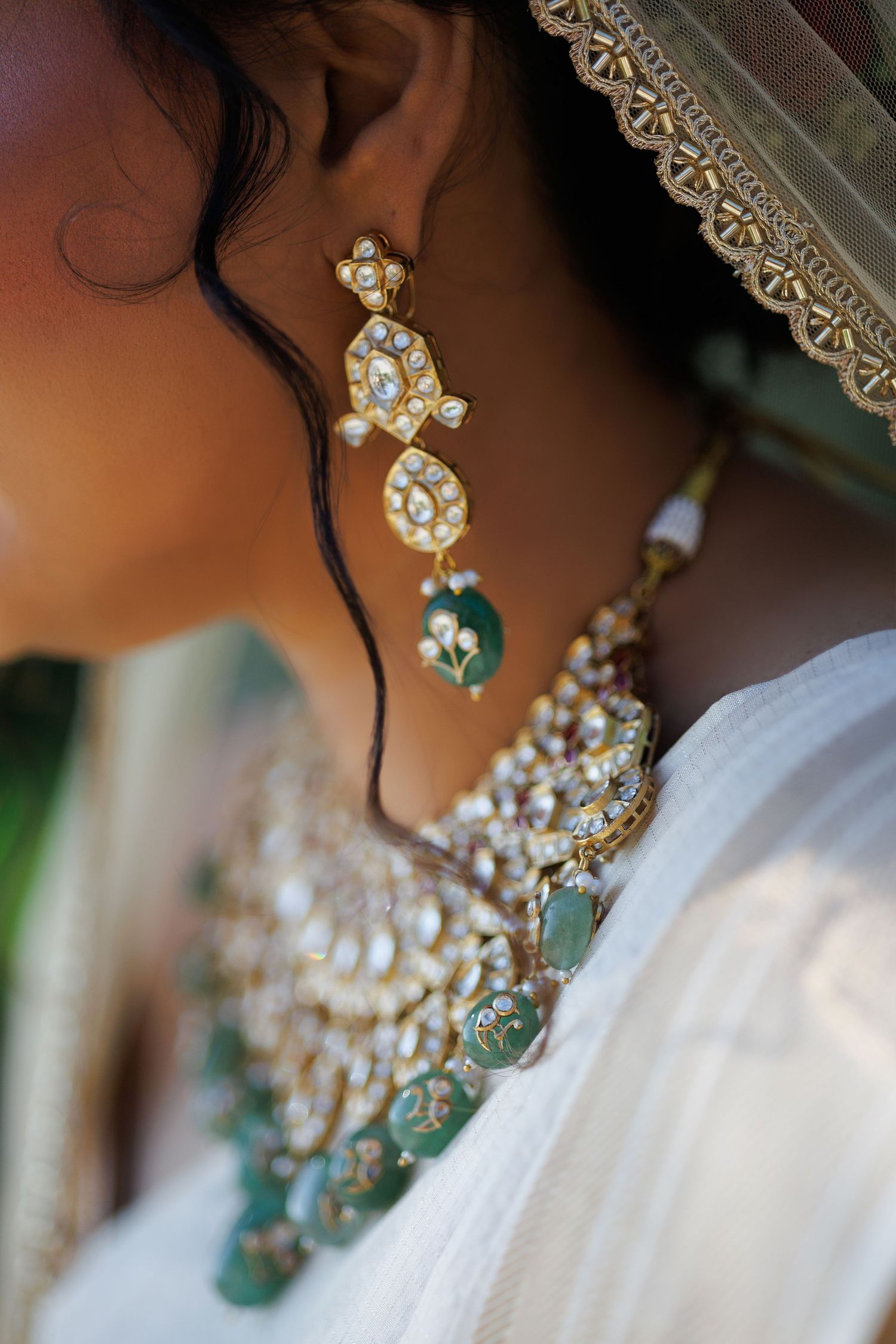 Close-up of a bride wearing traditional gold kundan jewelry with green stones, including ornate earrings and necklace.