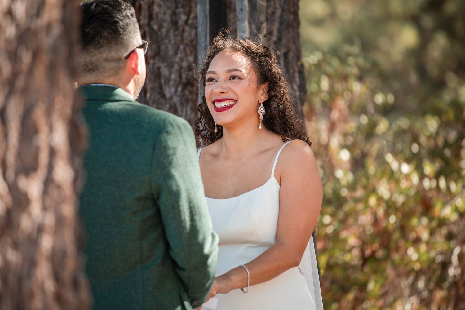 Joyful wedding couple shares intimate moments in a sun-dappled forest setting with natural lighting.