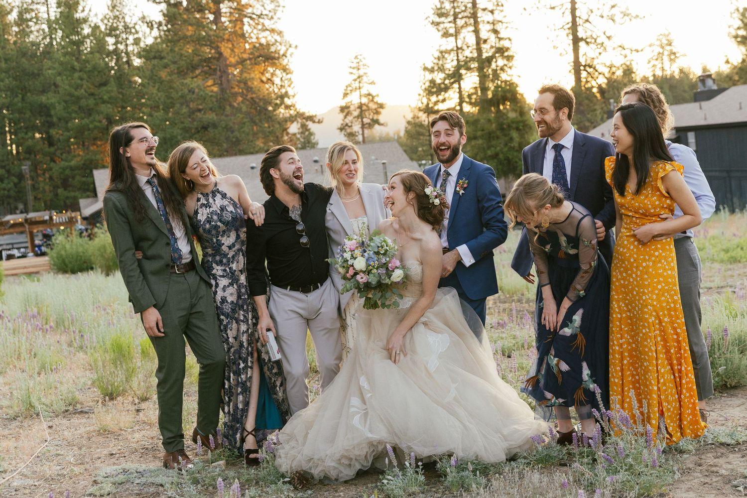 Wedding party celebrating outdoors with pine trees in background at sunset.