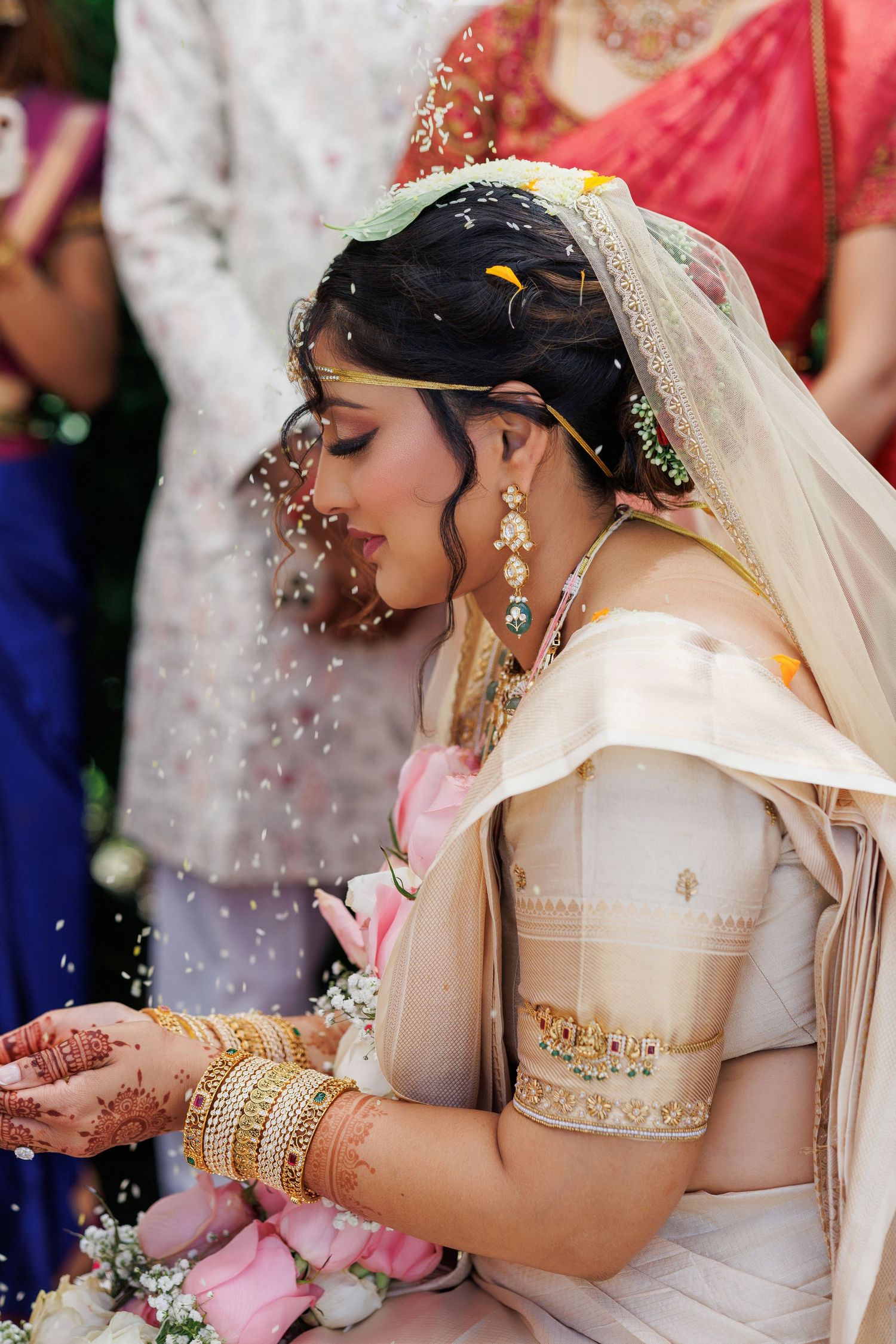 Beautiful Indian bride in cream saree with gold bangles and mehndi during Hindu wedding ceremony.