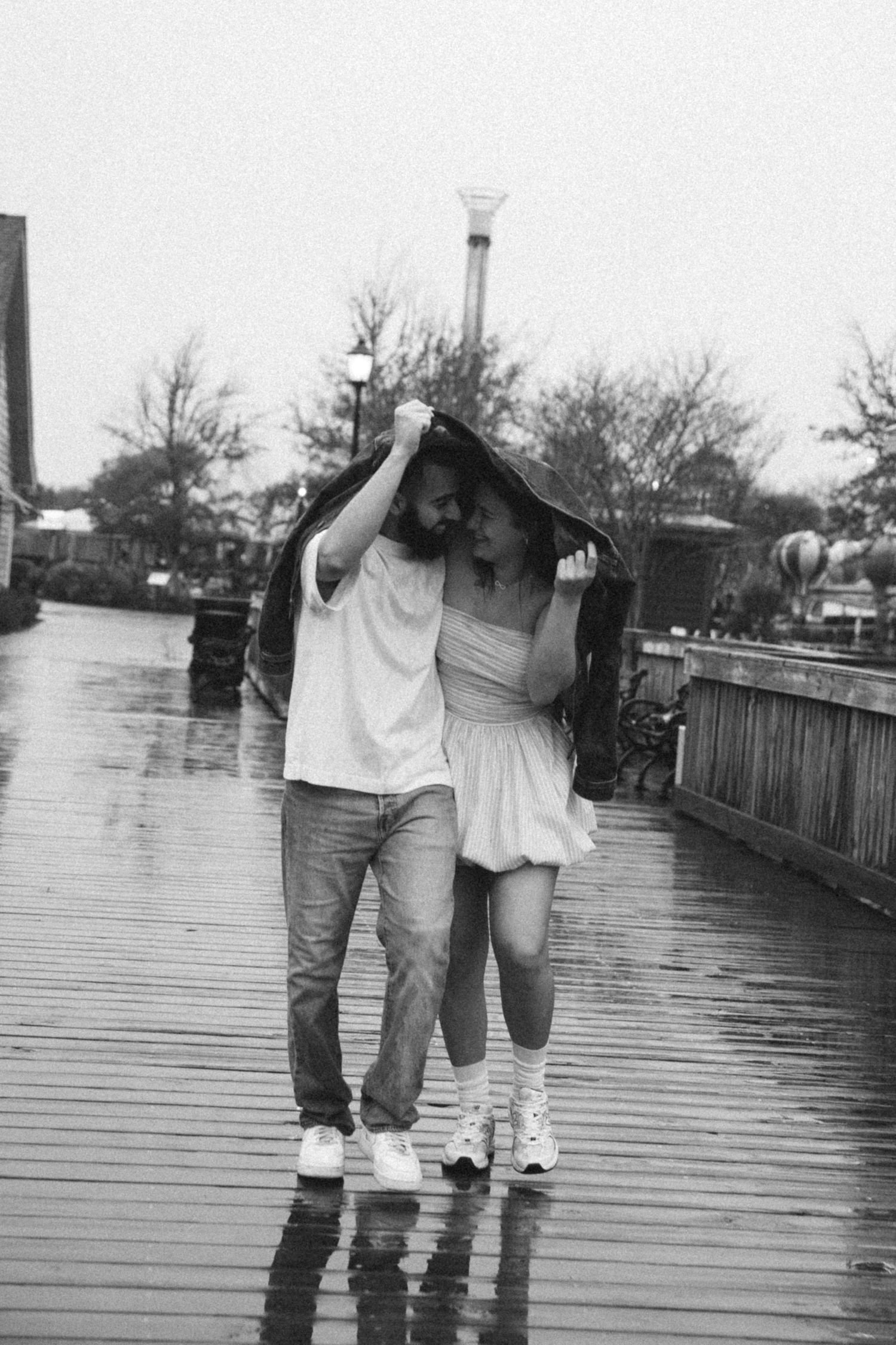 Black and white sequence of two people walking and splashing in puddles on a wooden boardwalk.