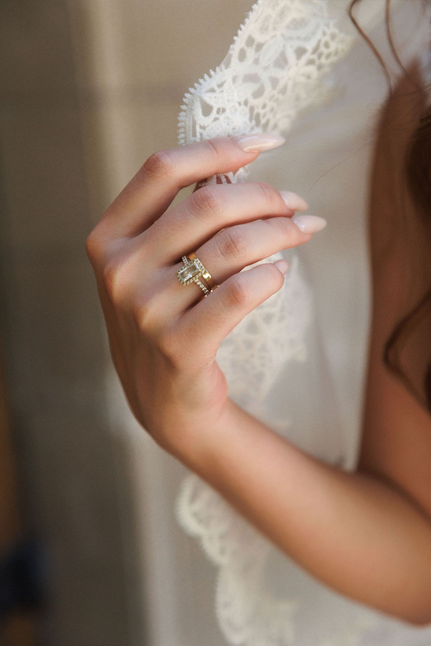 Close-up of bride's hand wearing gold engagement and wedding rings holding lace veil.