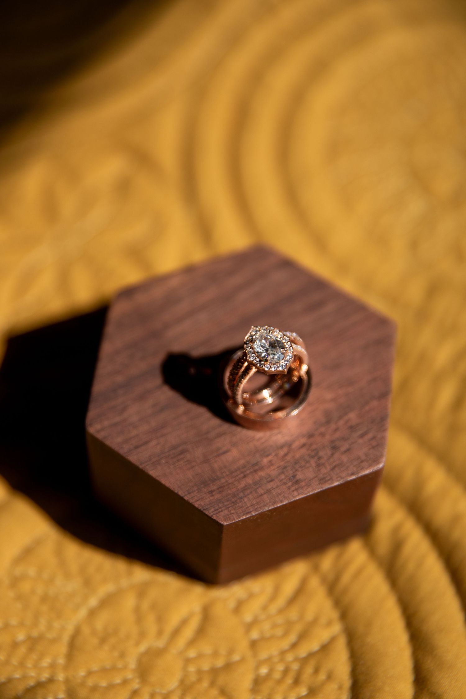 Close-up sequence of a diamond engagement ring being placed into a dark wooden hexagonal box on golden fabric.