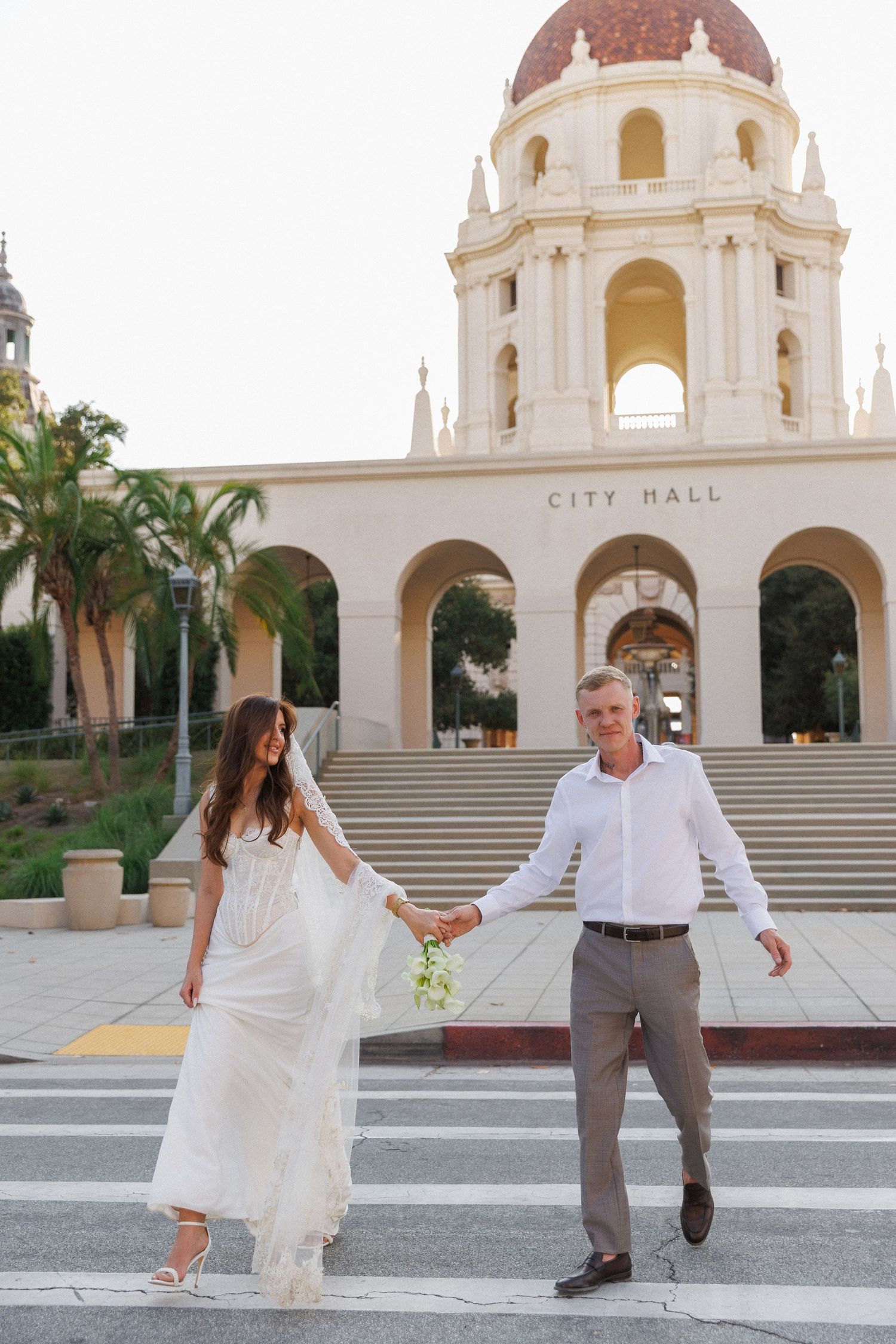 Bride and groom holding hands crossing street in front of Pasadena City Hall on their wedding day.