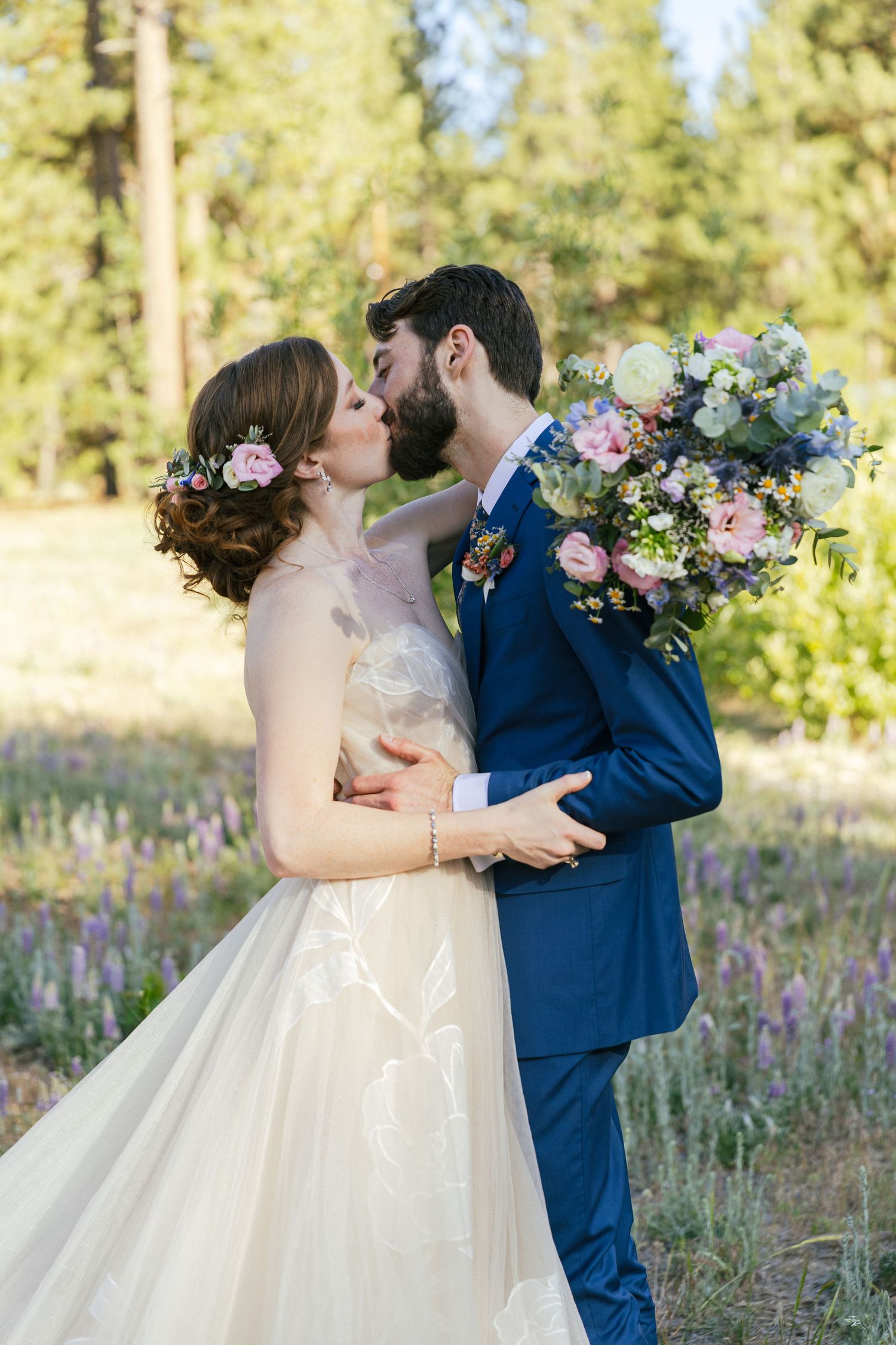 Newlyweds share intimate moments among wildflowers with bride in white gown and groom in navy suit.