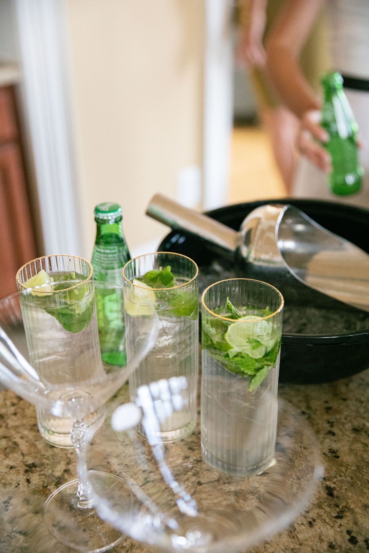 Glass tumblers with fresh mint leaves and beverages arranged on granite countertop.