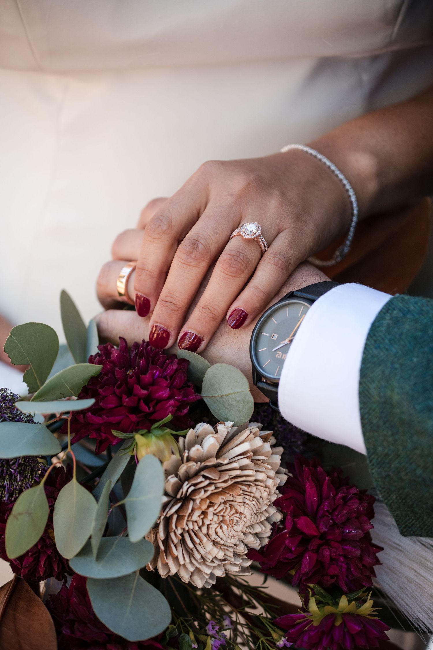 Hands arranging burgundy and beige flowers with eucalyptus leaves into a floral arrangement.