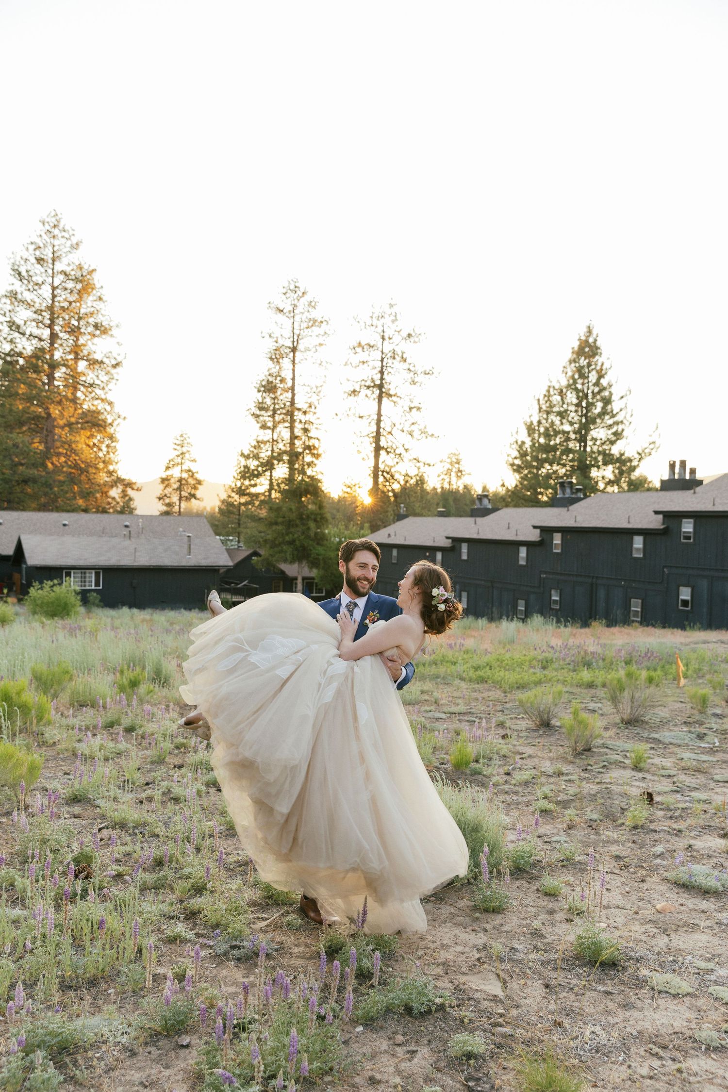 Playful wedding portraits in a field with dramatic dress movement and natural scenery.