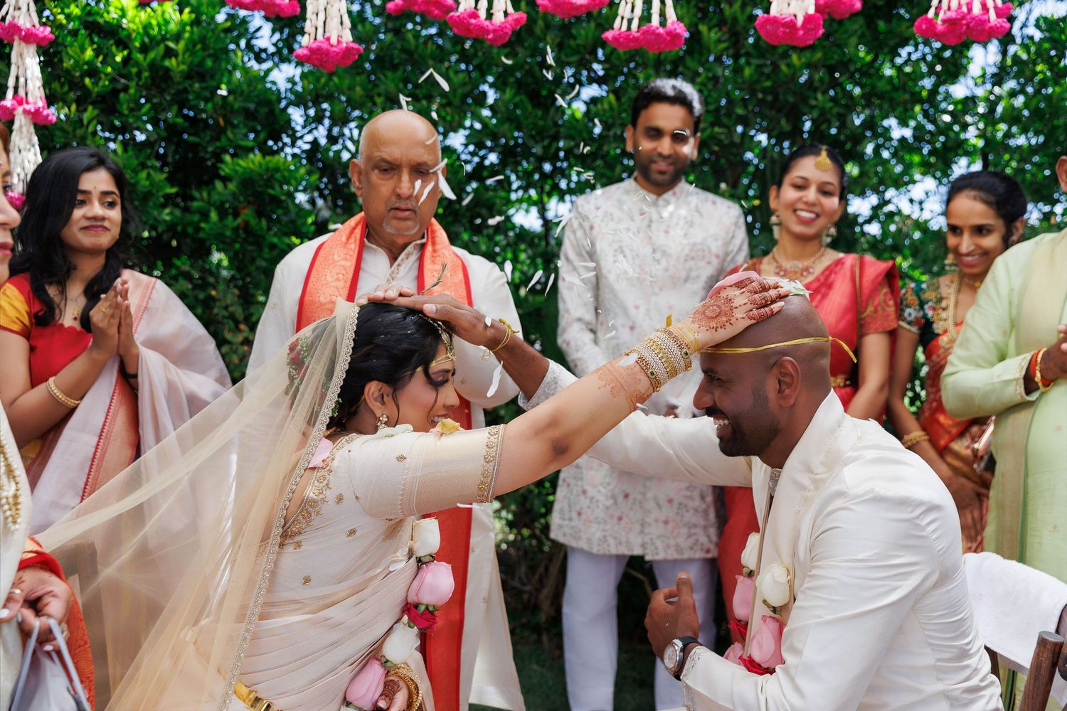 Bride and groom exchange garlands during a traditional Indian wedding ceremony outdoors with guests watching.