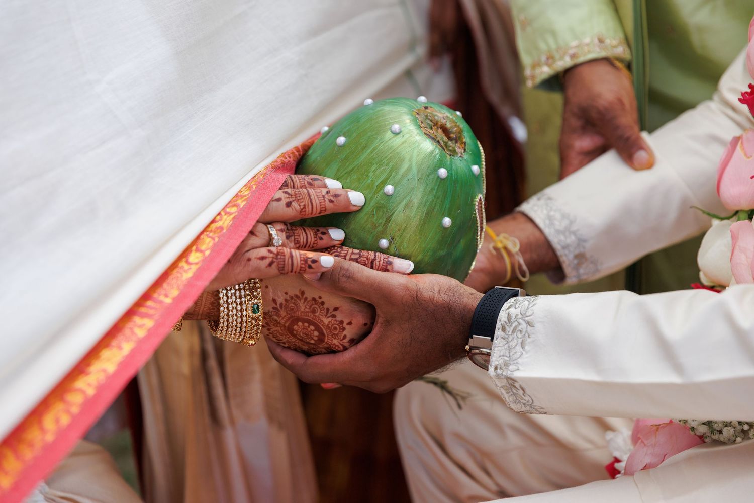 Bride and groom exchange green coconut during traditional Indian wedding ceremony with henna-adorned hands.