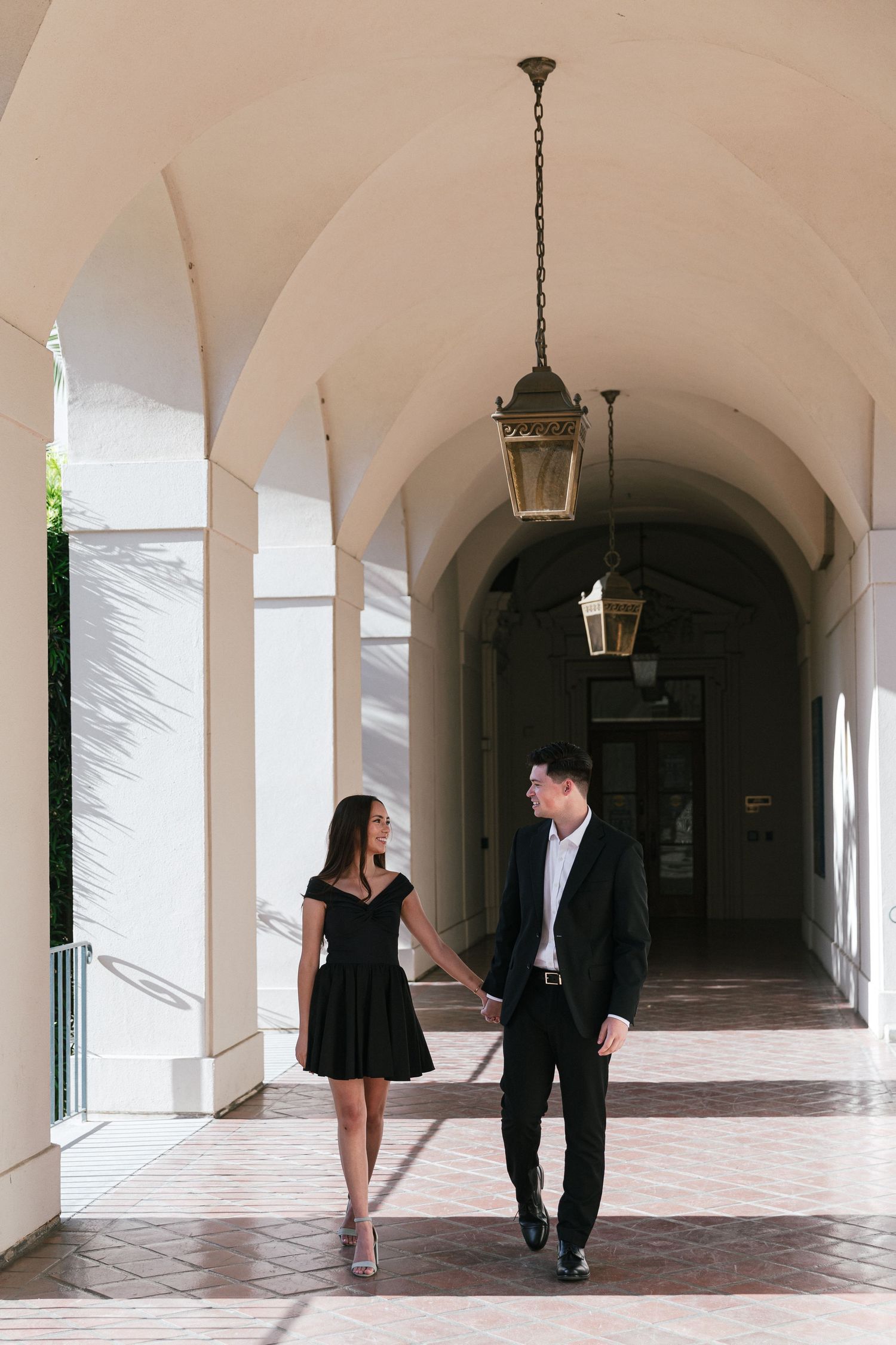 A couple poses beneath arched walkways and hanging lanterns in a Spanish colonial courtyard.