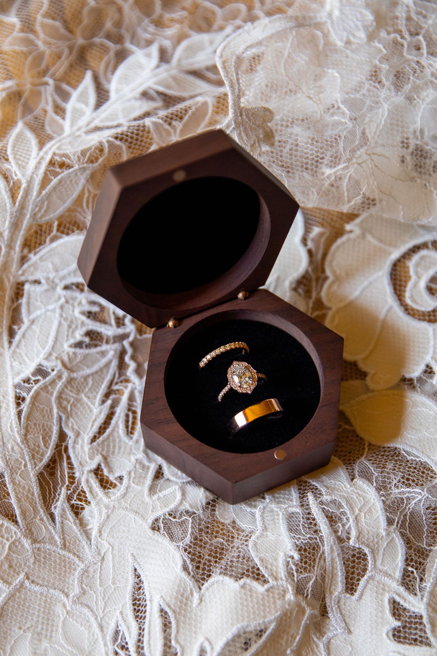 Two wedding rings displayed in dark brown wooden boxes on delicate white lace fabric.