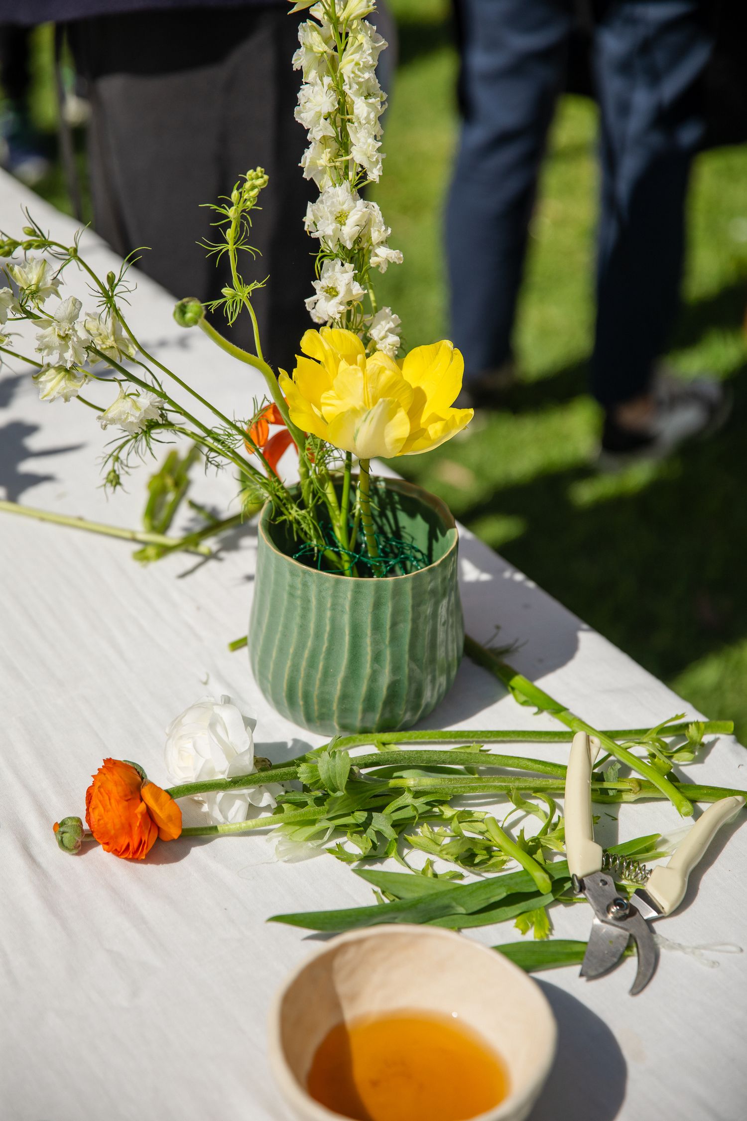 Close-up of floral arrangements in green vases with yellow and orange blooms on a white tablecloth.