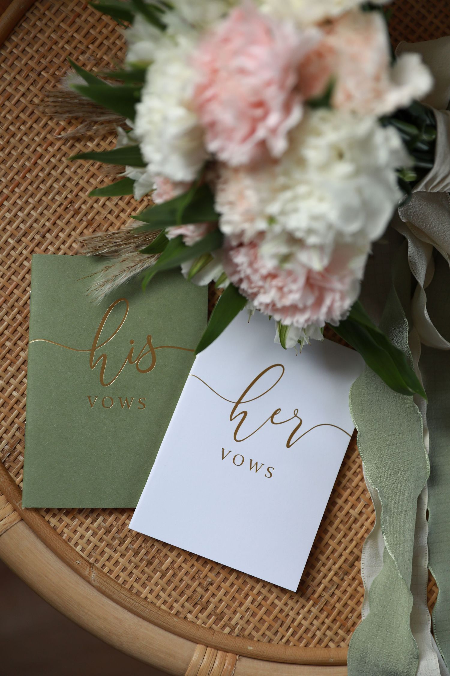 Wedding vow cards with elegant gold lettering displayed alongside pink and white flowers on burlap.
