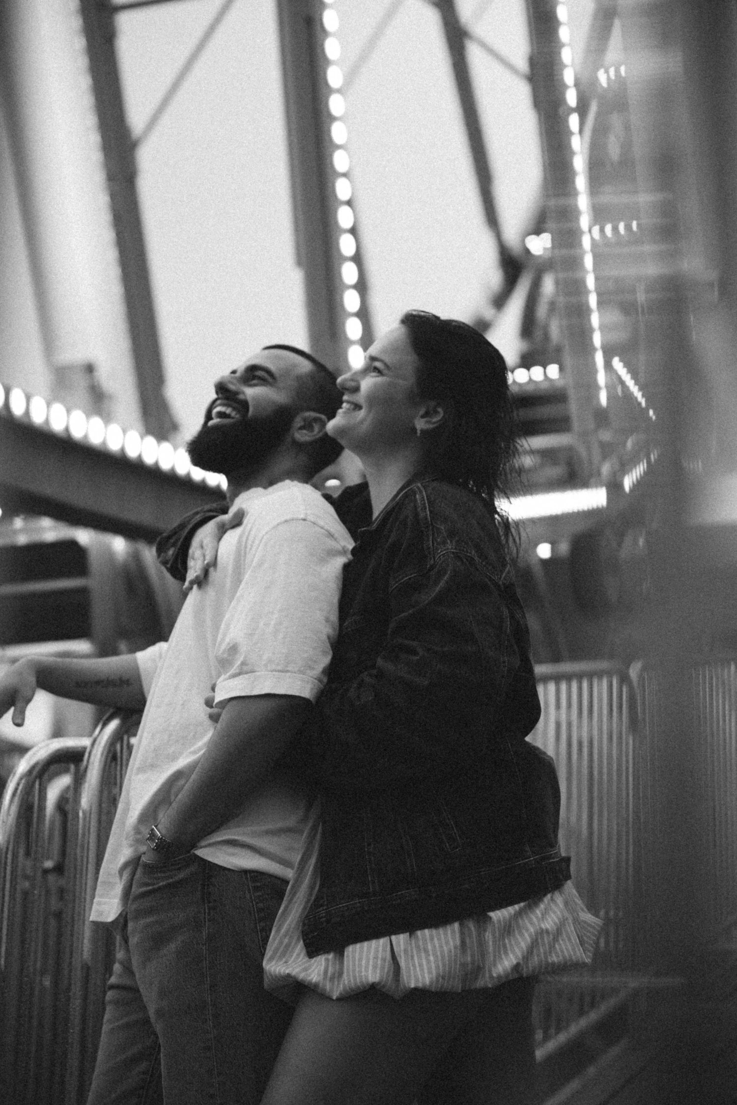 Black and white photos showing a couple leaning back against carnival railings at night.