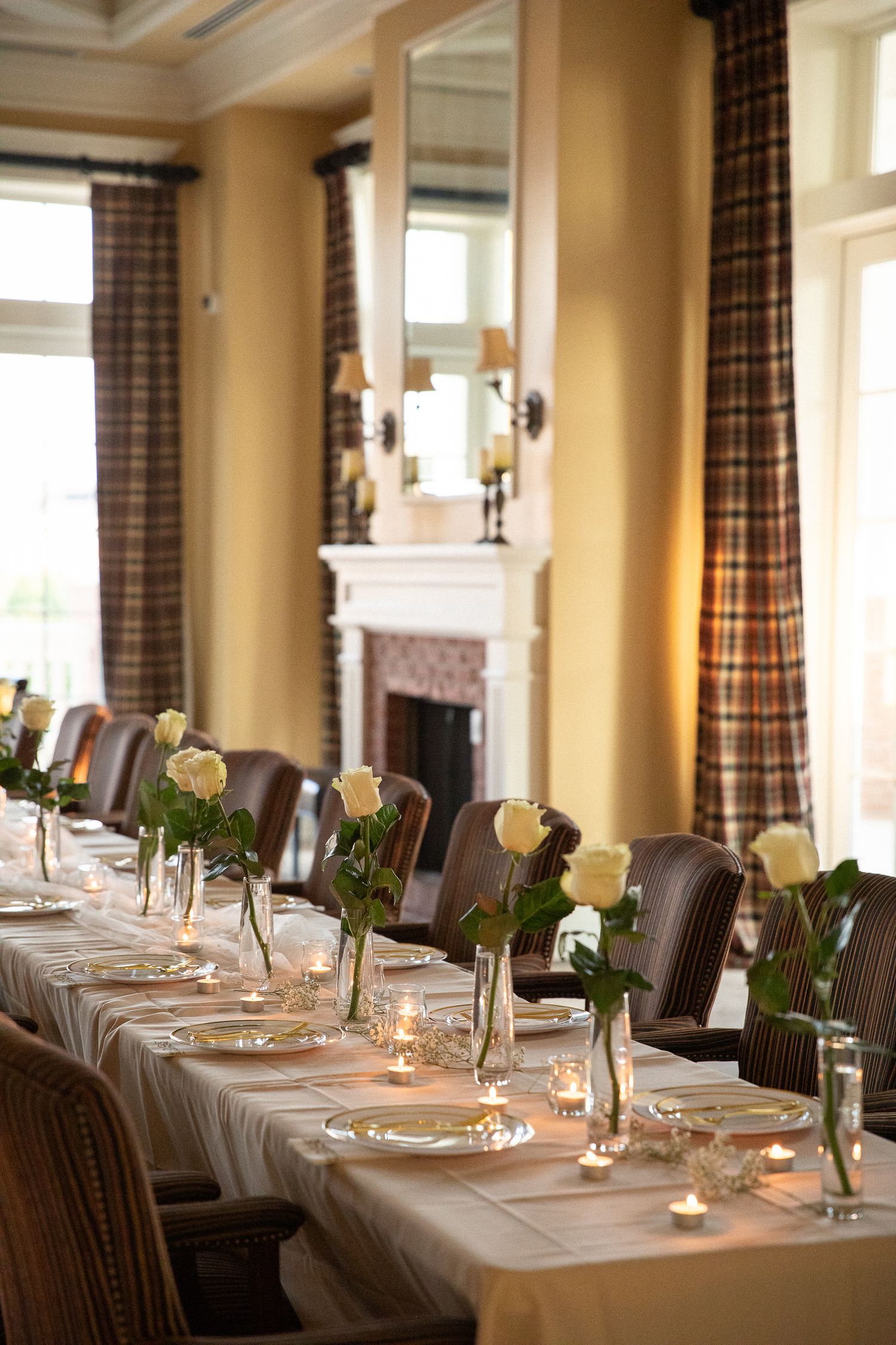 Elegant dining table set for a formal event with roses and plaid curtains in a stately room.