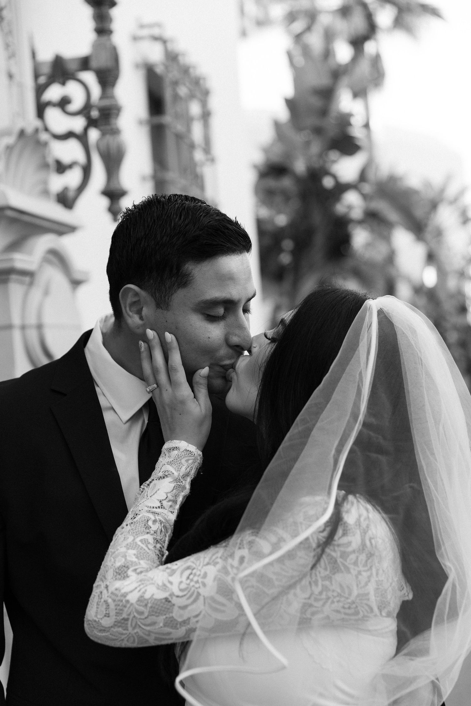 Black and white photo of a bride and groom sharing a romantic kiss, bride in lace dress and veil.