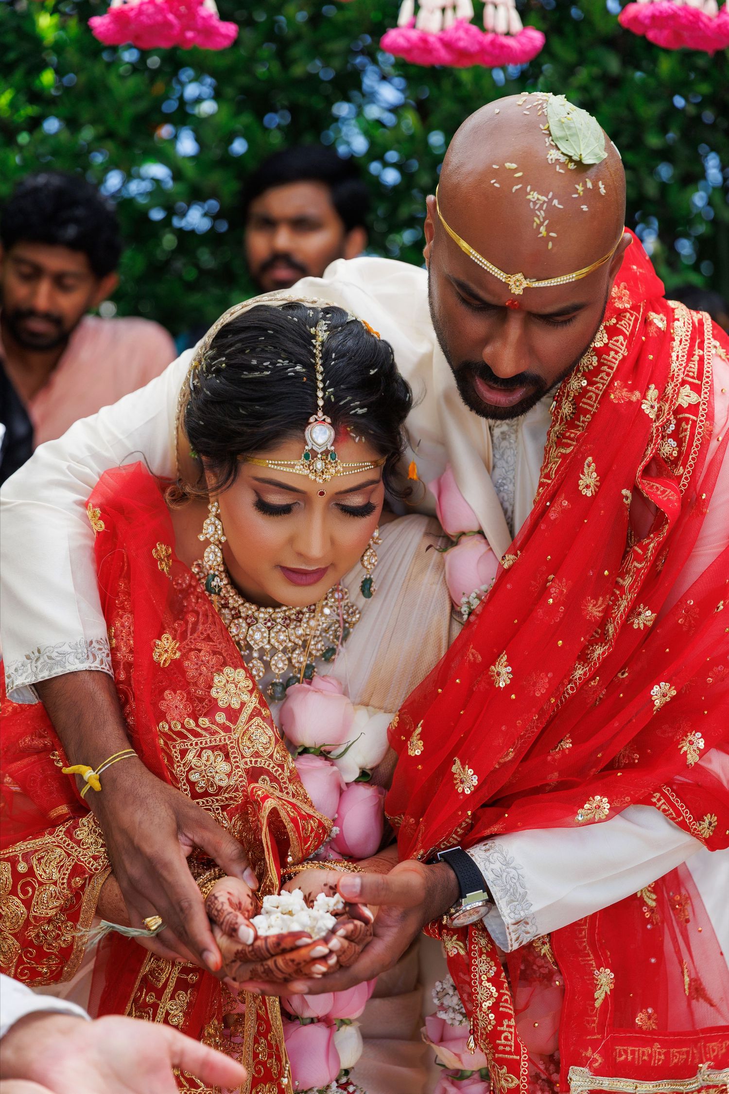 Indian bride and groom in traditional red and white attire performing Hindu wedding ritual ceremony outdoors.