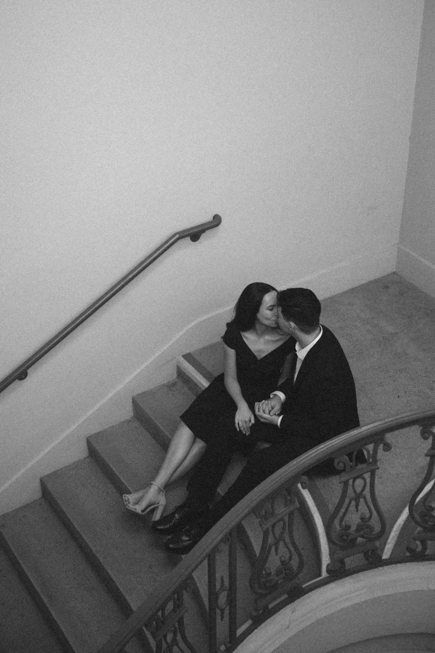 A romantic black and white photo of a couple sitting intimately on elegant curved stairs.