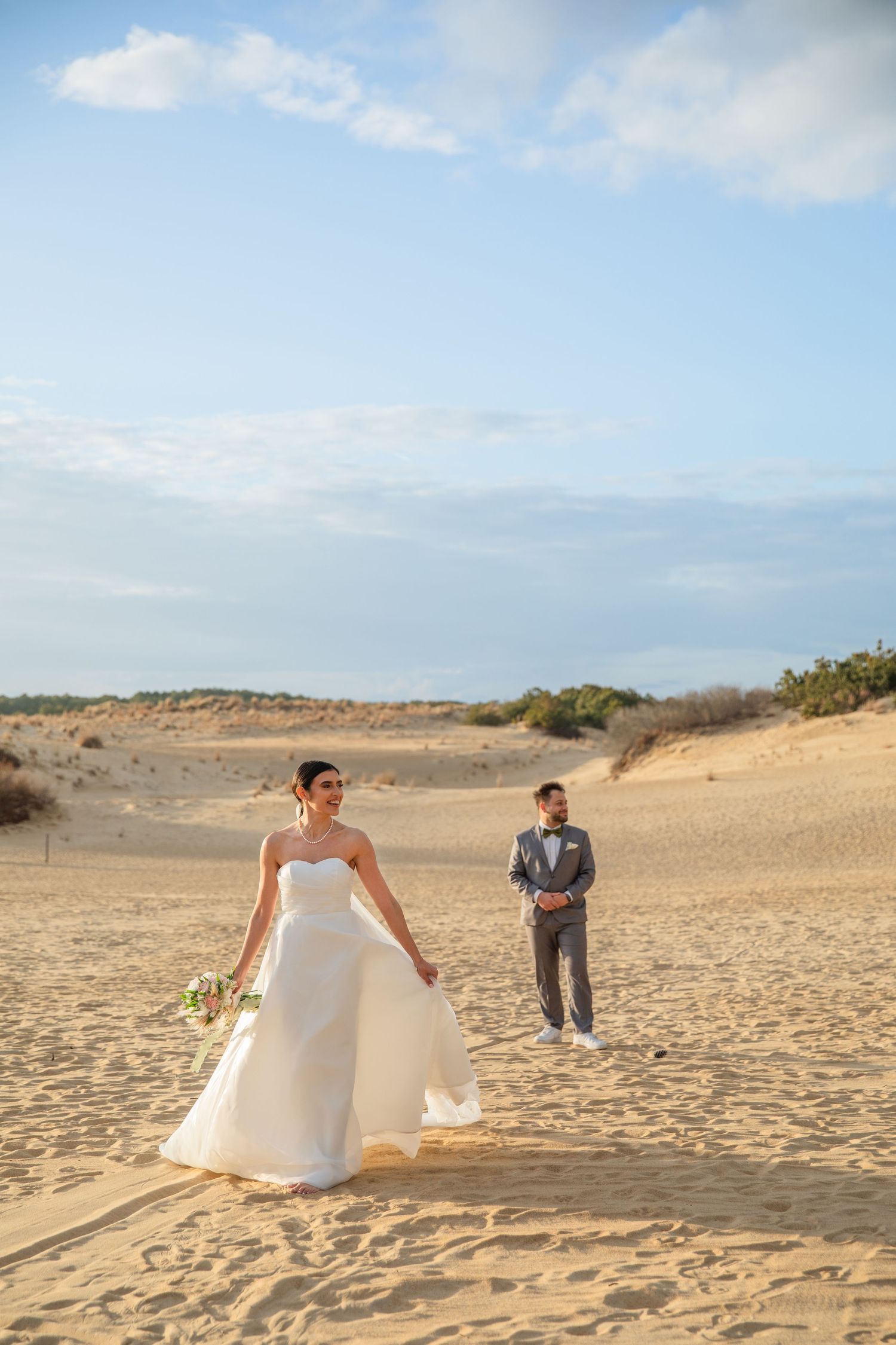 A wedding photoshoot takes place on scenic sand dunes under blue skies.