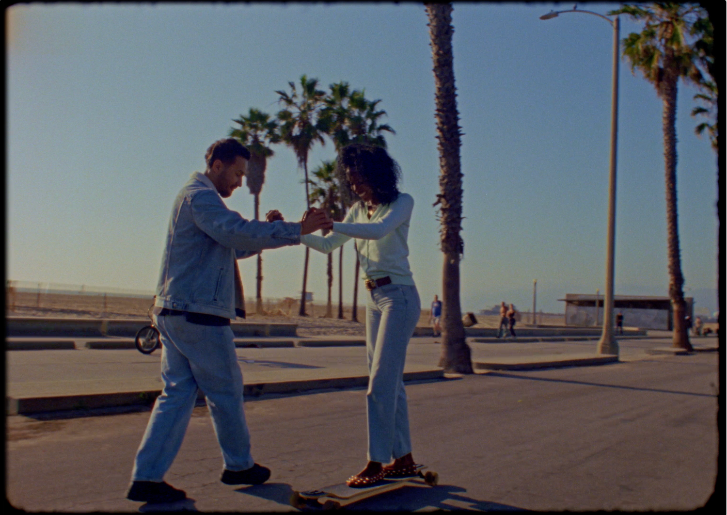 A romantic marriage proposal scene unfolds on a palm tree-lined beach boardwalk at sunset.