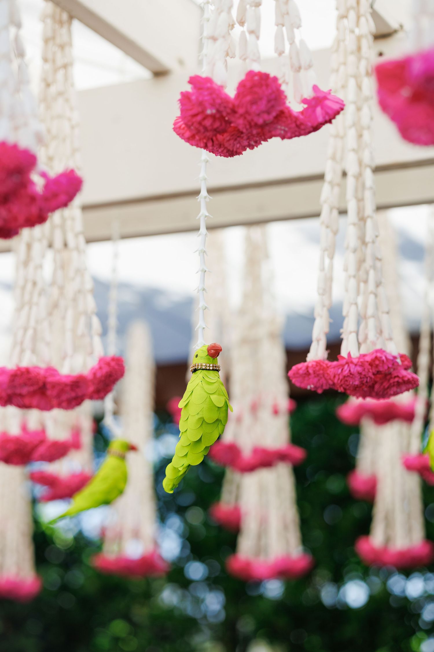 Decorative hanging ornaments with pink floral clusters, white tassels, and a green parrot figurine for festive decor.