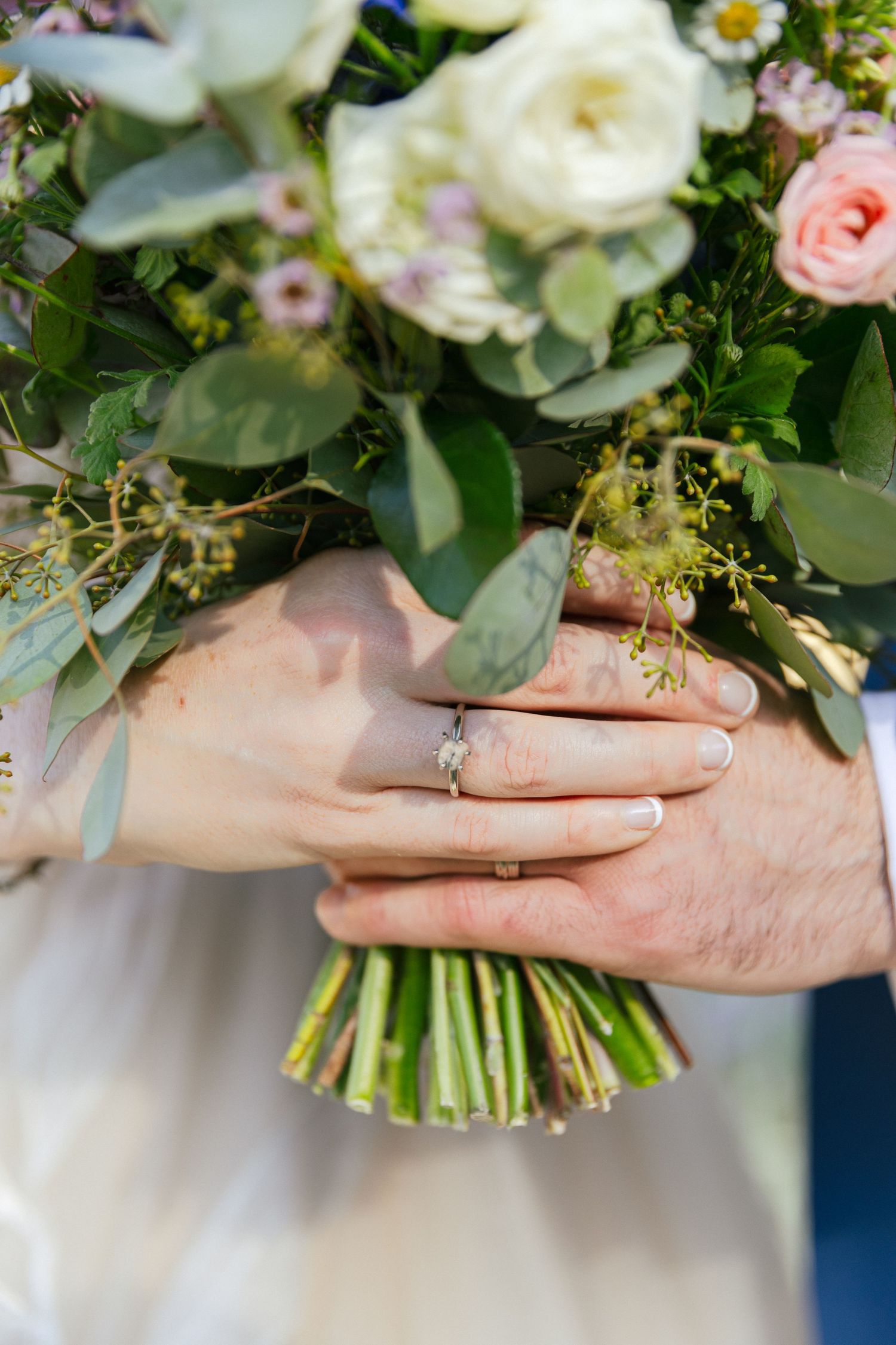 Close-up view of hands holding a delicate bridal bouquet with white and pink roses wrapped in green foliage.