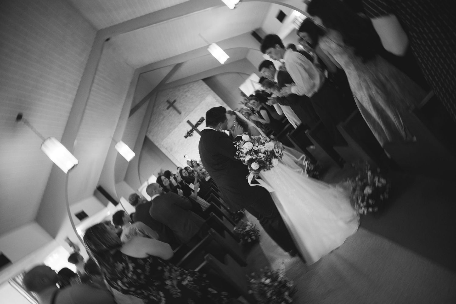 Black and white photo of a wedding ceremony inside a church with bride, groom, and wedding party at the altar.