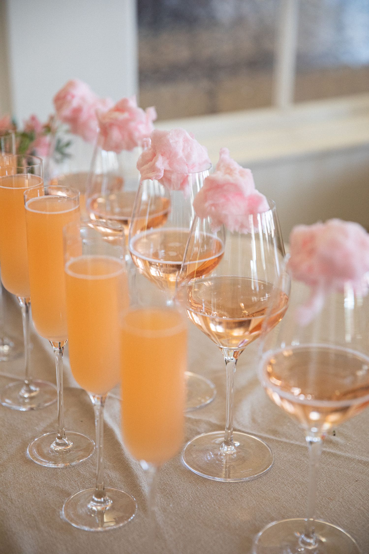 Row of cocktail glasses filled with orange drinks and topped with pink cotton candy garnishes.
