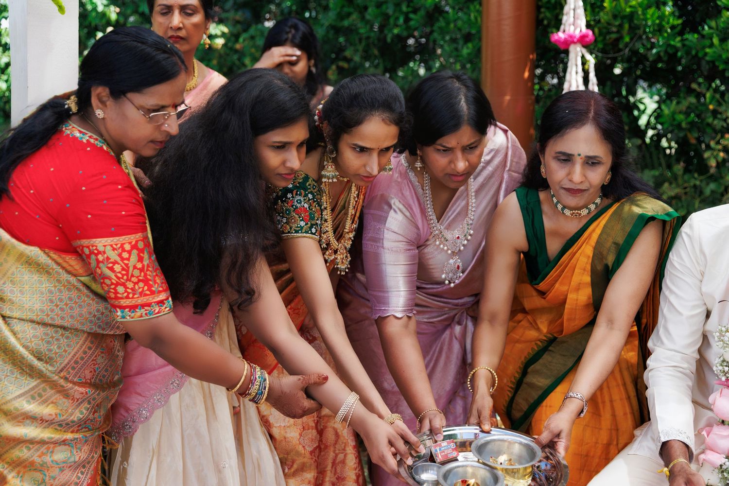 Indian women in traditional sarees performing a cultural ritual ceremony together outdoors.