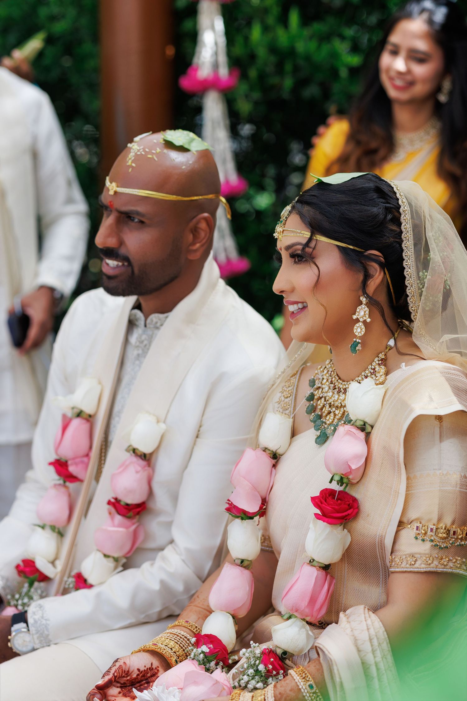 Bride and groom in traditional Indian wedding attire with floral garlands during a Hindu marriage ceremony outdoors.