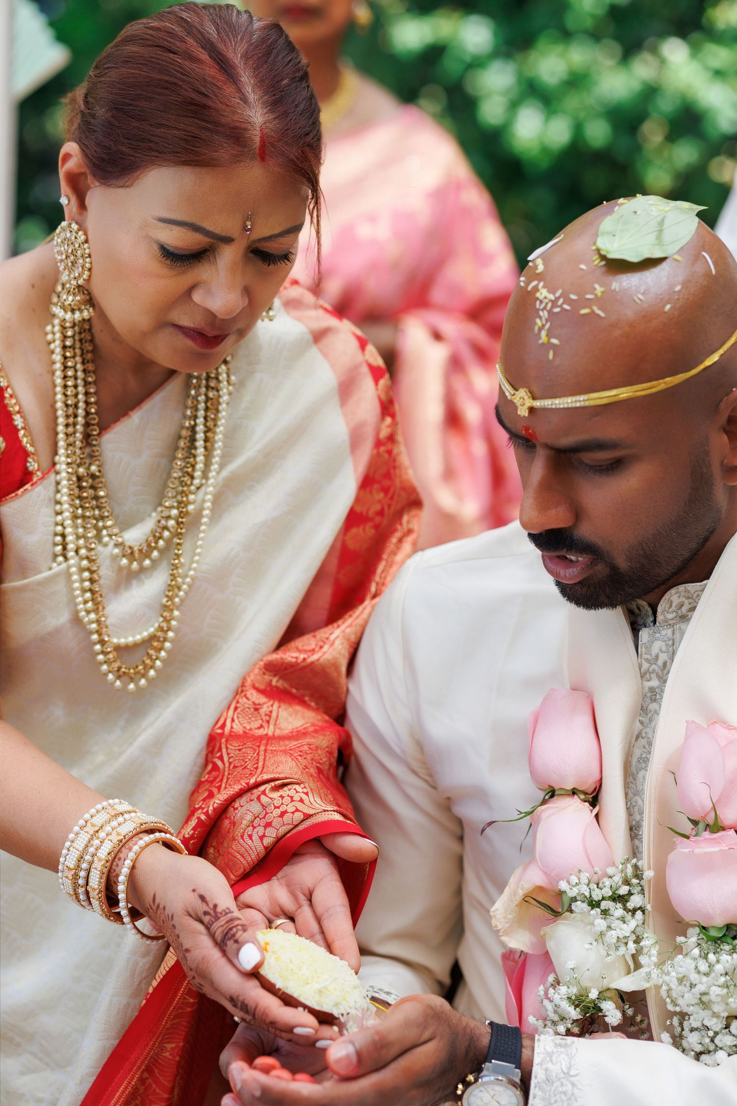 Indian wedding ceremony couple in traditional white and red attire exchanging ritual offerings outdoors.