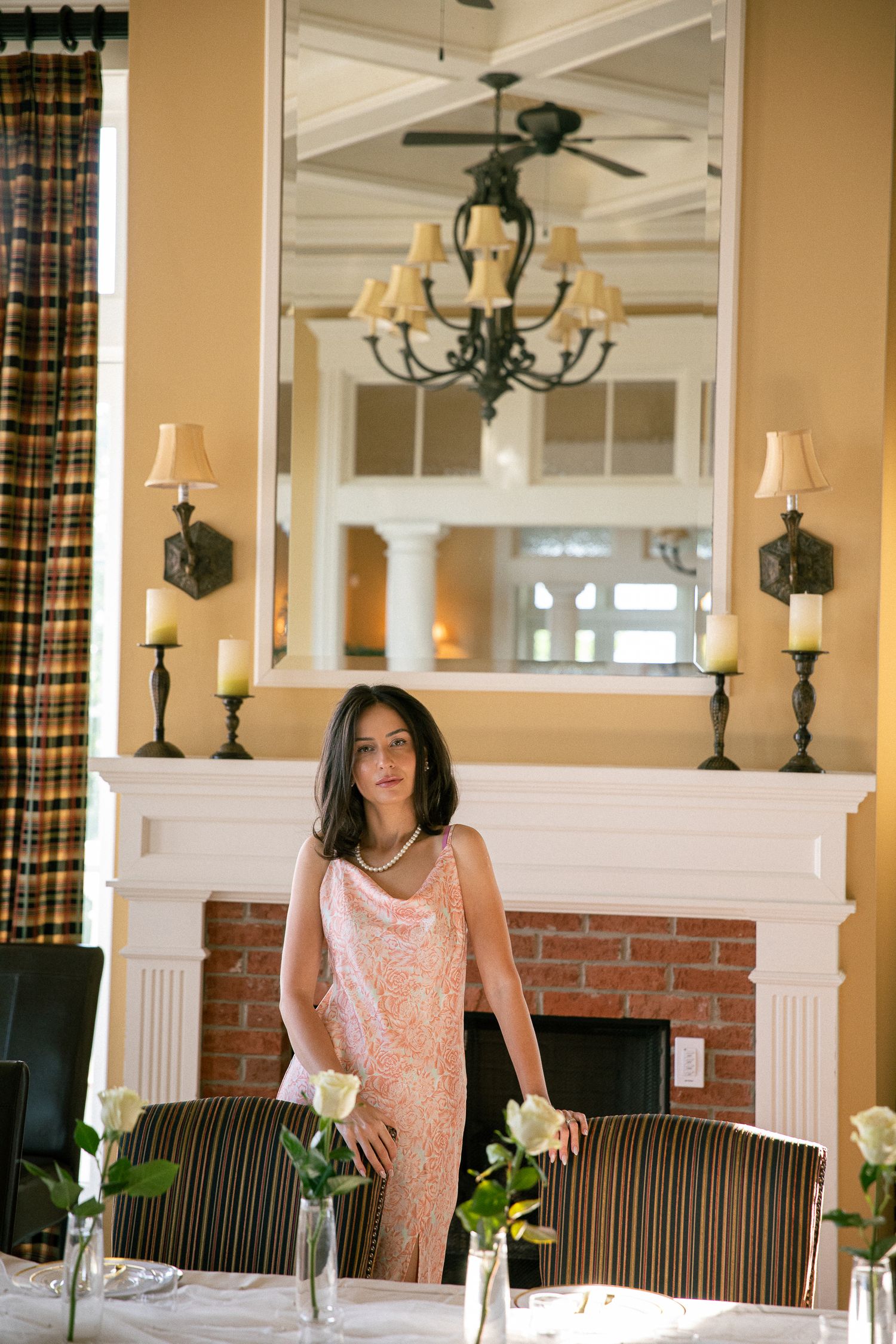 A pink lace dress is showcased in an elegant interior setting with striped chairs and chandeliers.