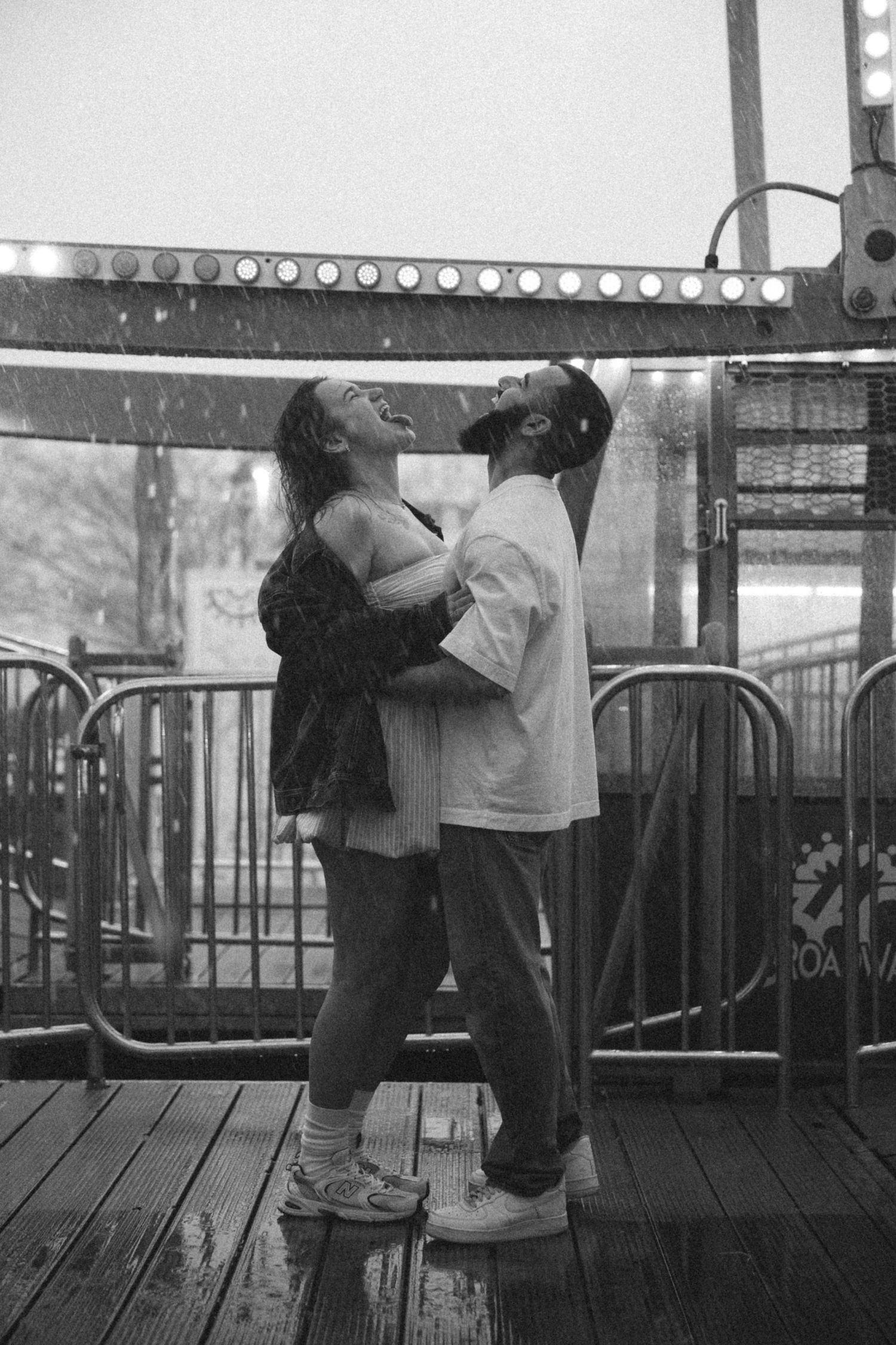 Intimate black and white sequence showing two people embracing on a boardwalk with carnival lights.