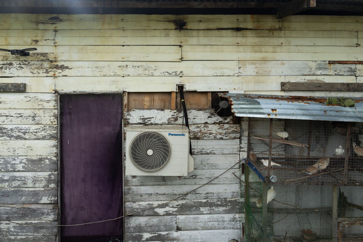 Some residents still enjoy the comfort of using air conditioning and the hobby of keeping birds in cages at one of the wooden houses