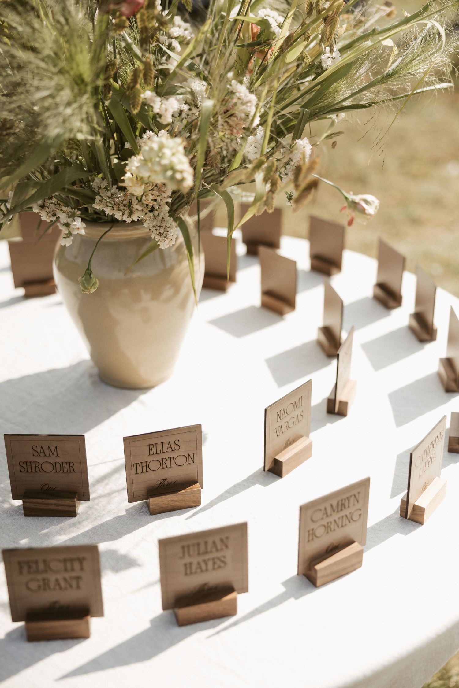 Wedding place cards with names displayed on wooden holders alongside delicate floral centerpieces in soft natural lighting.