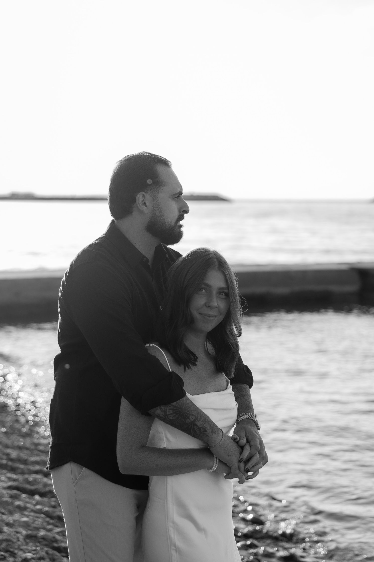 A couple embraces lovingly by the ocean shore during a black and white photo session.