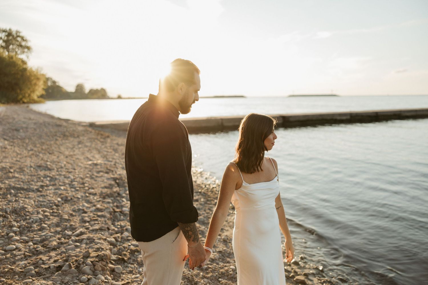 Couple walking hand in hand along rocky shoreline at sunset.